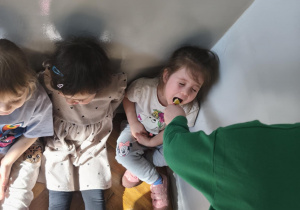 Na zdjęciu widzimy dziewczynkę, która z zamkniętymi oczami próbuje kawałka pomarańczy.