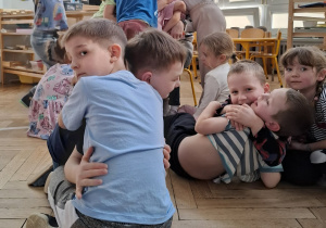 dzieci przytulają się do siebie i kobiety, która czytałą im książkę