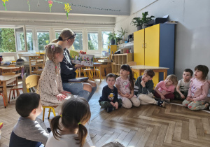 Na zdjęciu widzimy mamę Anastazji, która czyta dzieciom książkę o Jadzi.