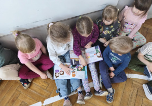 Na zdjęciu widzimy dzieci, które oglądają ilustracje w książkach czytanych przez mamę Anastazji.