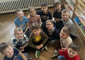 Zdjęcie przedstawia dziewczynkę siedzącą wśród chłopców.