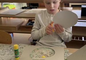 Zdjęcie przedstawia chłopca podczas wykonywania pracy plastycznej. Chłopiec wycina koło.