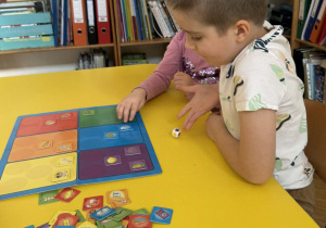 Zdjęcie przedstawia dzieci siedzące przy stoliku, podczas gry w grę planszową.