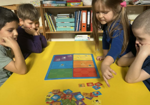 Zdjęcie przedstawia dzieci siedzące przy stoliku, podczas gry w grę planszową.