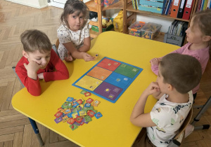 Zdjęcie przedstawia dzieci siedzące przy stoliku, podczas gry w grę planszową.