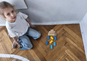 Na zdjęciu widzimy dziewczynkę, która z klcoków drewnianych zrobiła chmurę z burzą.