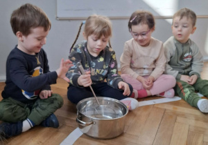 Na zdjęciu widzimy dziewczynkę, która miesza ilustrację pogody marcowej w garnku za pomocą łyżki.