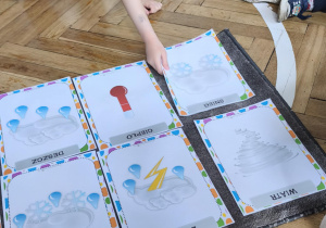 Na zdjęciu widzimy dziewczynkę, która kładzie na dywanik ilustrację przedstawiającą śnieg.