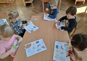 Na zdjęciu widzimy dzieci, które wycinają ilustrację przedstawiające różne stany pogody marcowej.
