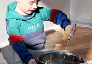 Na zdjęciu widzimy chłopca, który miesza ilustrację pogody marcowej w garnku za pomocą łyżki.