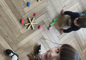 Na zdjęciu widzimy dziewczynkę, która wykonała słonko z klocków drewnianych oraz dziewczynkę i chłocpa, którzy tworzą własne prace.