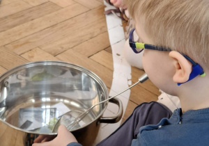 Na zdjęciu widzimy chłopca, który miesza ilustrację pogody marcowej w garnku za pomocą łyżki.