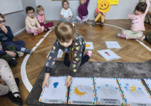 Na zdjęciu widzimy dziewczynkę, która kładzie na dywanik ilustrację przedstawiającą stan pogody - zimno.