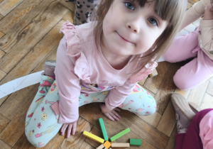 Na zdjęciu widzimy dziewczynkę, która z klcoków drewnianych zrobiła słoneczko.