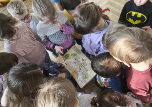 Na zdjęciu widzimy dzieci, które oglądają ilustrację w książce.