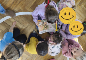 Na zdjęciu widzimy dzieci, które oglądają ilustrację w książce.