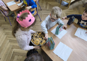 Na zdjęciu widzimy Jubilatkę, która częstuje babeczką chłopca.