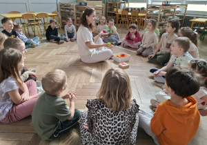 kobieta siedzi przed dziećmi, w rękach trzyma kolorowe klocki