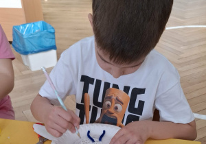 chłopiec przy stole tworzy królika z papieru