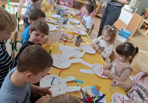 dzieci przy stołach tworzą królika z papieru