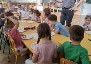 grupa dzieci siedzi przy stole, słuchają kobiety