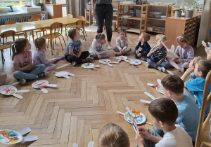 dzieci siedzą na elipsie, przed nimi leżą gotowe króliki, słuchają kobiety