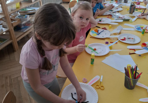 dzieci przy stołach tworzą królika z papieru