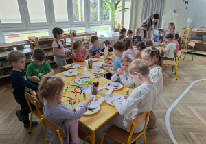 dzieci przy stołach tworzą królika z papieru