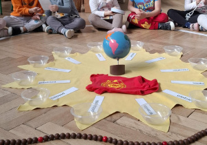 dzieci siedzą na elipsie, oglądają zdjęcia i pamiątki z wczesnego dzieciństwa kolegi