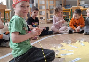 chłopiec w czerwonej koronie nawleka korale na sznurek