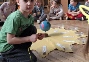 chłopiec w czerwonej koronie nawleka korale na sznurek