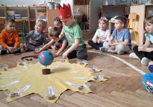 chłopiec w czerwonej koronie nawleka korale na sznurek