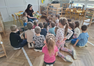 dzieci siedzą przed kobietą, która czyta książkę