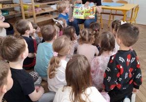 dzieci siedzą przed kobietą, która czyta książkę