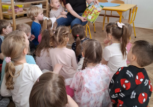 dzieci siedzą przed kobietą, która czyta książkę