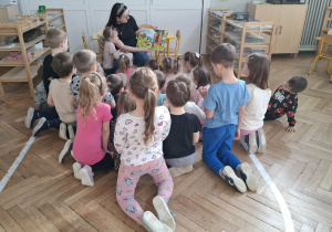 dzieci siedzą przed kobietą, która czyta książkę