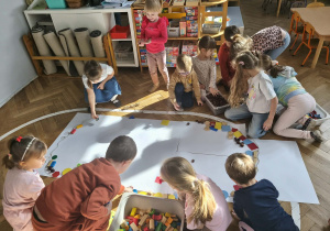 Na zdjęciu widzimy dzieci, które z wykorzystaniem klocków oraz materiału przyrodniczego tworzą wielką pisankę.