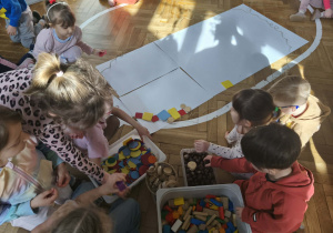 Na zdjęciu widzimy dzieci, które z wykorzystaniem klocków oraz materiału przyrodniczego tworzą wielką pisankę.