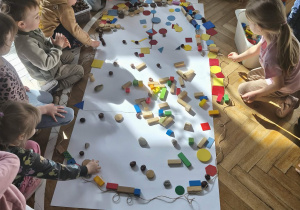 Na zdjęciu widzimy dzieci, które z wykorzystaniem klocków oraz materiału przyrodniczego tworzą wielką pisankę.