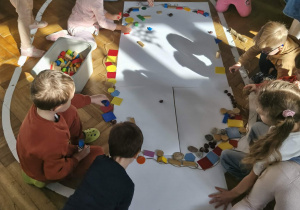 Na zdjęciu widzimy dzieci, które z wykorzystaniem klocków oraz materiału przyrodniczego tworzą wielką pisankę.