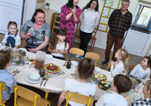 Na zdjęciu widzimy dzieci siedzące przy stole oraz personel przedszkola wraz z panią Dyrektor.