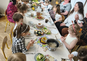 Na zdjęciu widzimy dzieci siedzące przy stole oraz personel przedszkola.