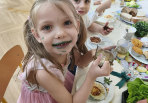 Na zdjęciu widzimy dziewczynkę, której buzia ubrudzona jest na zielono po zjedzeniu babeczki.