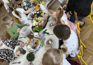 Na zdjęciu widzimy dzieci, które siedzą przy wielkanocnym stole i jedzą śniadanie.