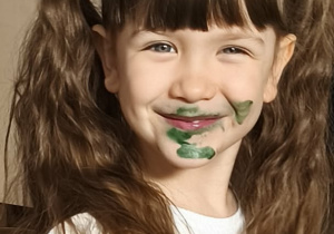 Na zdjęciu widzimy dziewczynkę, której buzia ubrudzona jest na zielono po zjedzeniu babeczki.