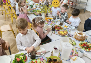 Na zdjęciu widzimy dzieci, które siedzą przy wielkanocnym stole i jedzą śniadanie.