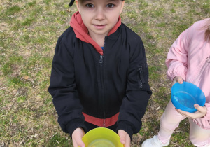 Na zdjęciu widzimy chłopca, który trzyma w ręku miseczkę z jajkiem czekoladowym.