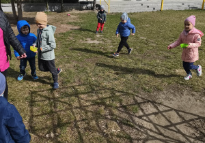 Na zdjęciu widzimy grupkę dzieci, które szukają jajeczek w ogrodzie przedszkolnym.
