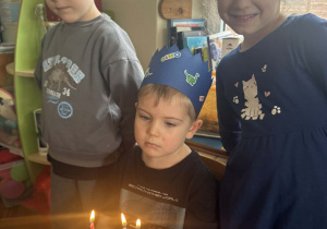 Zdjęcie przedstawia chłopca obok tortu z zapalonymi świeczkami.