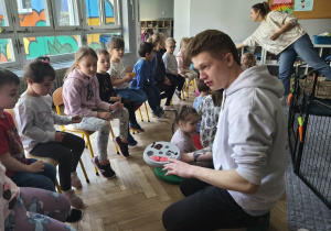 Na zdjęciu widzimy Pana, który pokazuje dzieciom zabawki dla królików.